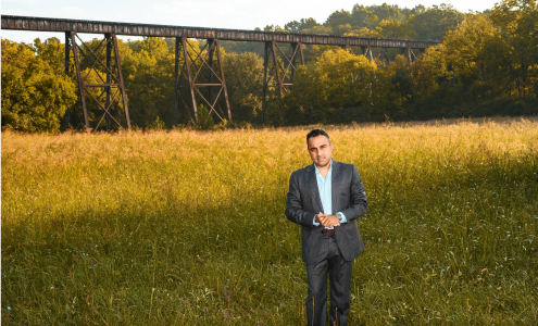 Ankur Gopal in a business suit standing in golden wheat or grain field with trees in background